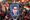 A large crowd of people participates in a political rally. Many in the crowd are holding up signs, including a large portrait