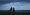 A silhouetted family of four stand on a beach in Sri Lanka, gazing at the ocean under a dark, stormy sky.