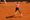 A photo of Sumit Nagal, Indian tennis player, in mid air as he prepares to receive a tennis ball. Sumit is playing on a red c