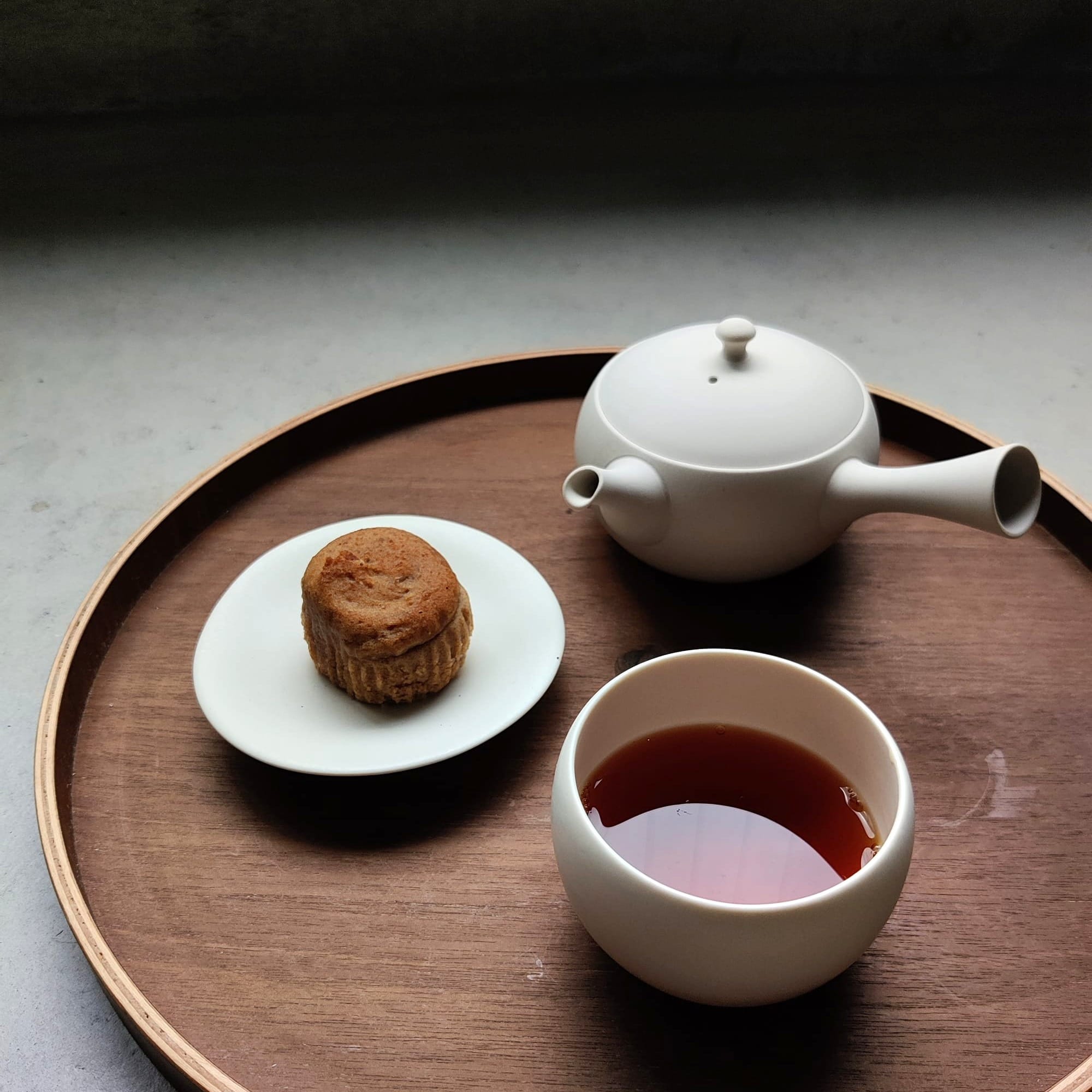 A photo of a white kyusu teapot, a cup of aged Japanese oolong tea and a treat on a tray. Photo credit: Jan (@janschanoma)