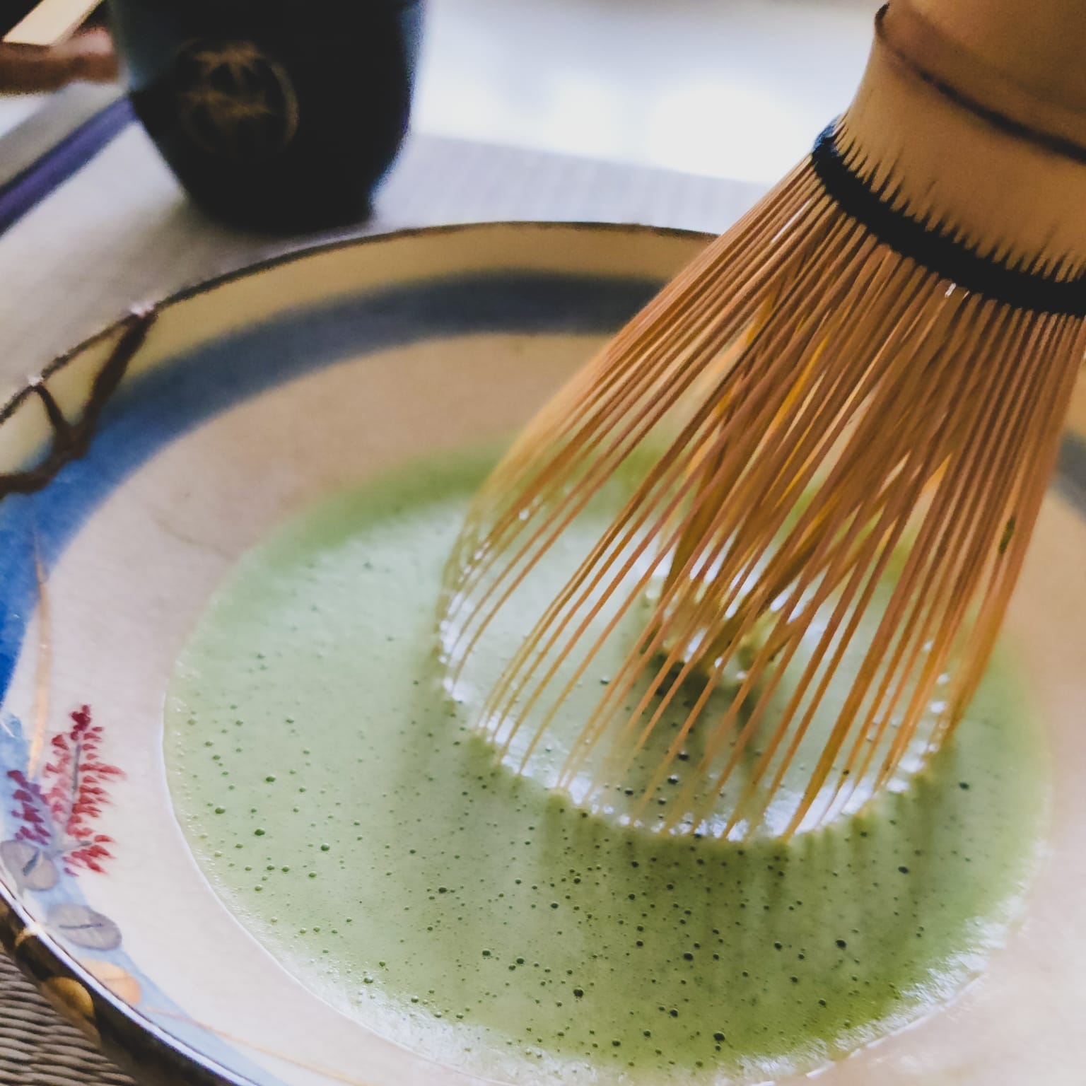 Close up photo of a chasen (bamboo whisk) whisking matcha in a bowl. Photo Credit @janschanoma