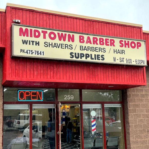 Storefront: red roof, Midtown Barber Shop sign. In window is an "Open" sign and decal of barber pole.
