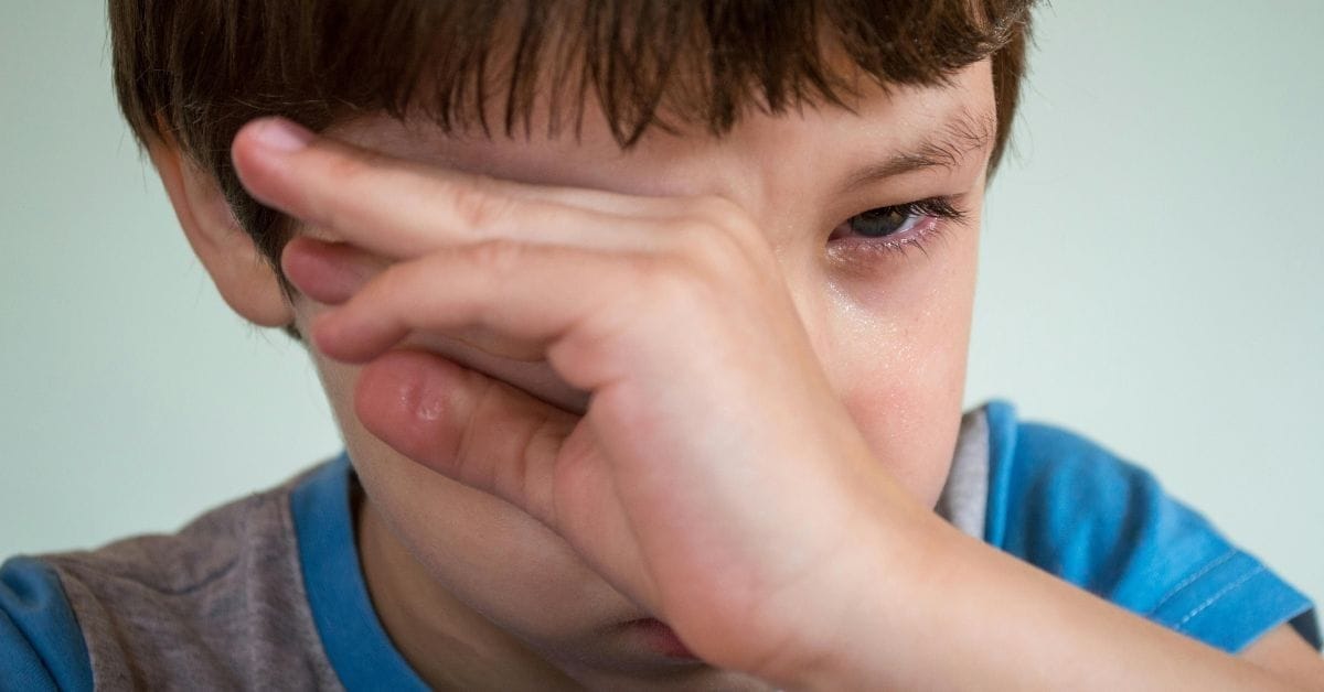 Crying boy wipes tears from his eyes.