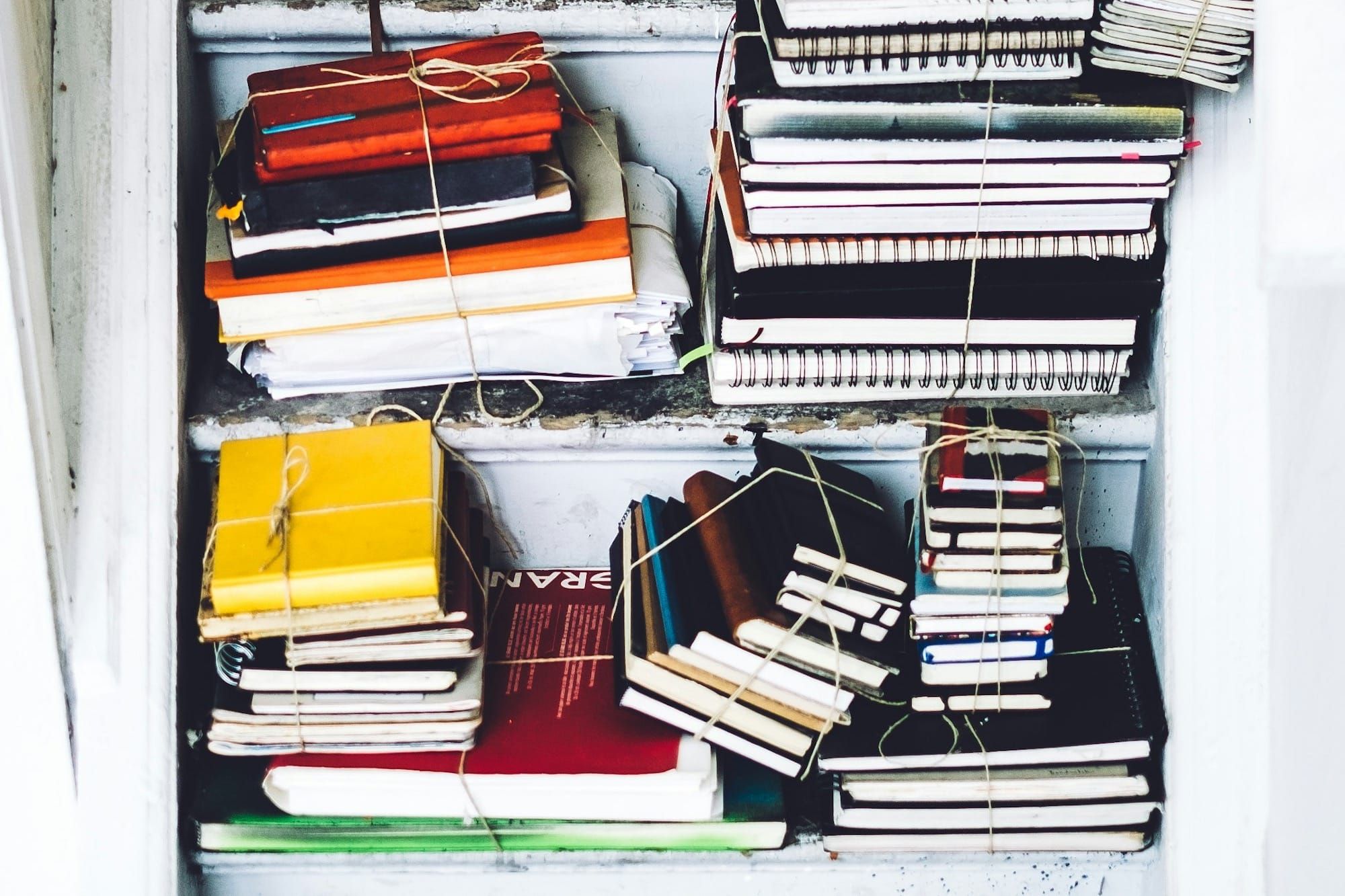 Stacks of used notebooks of different sizes and models, held together by string.