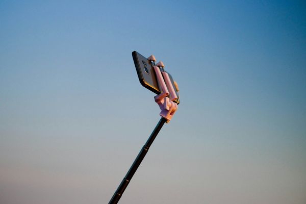 A selfie stick holding an Android phone against a blue, clear sky.