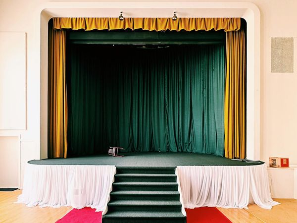 A small empty stage in a bright space, draped with outdated textiles in yellow, green and white.