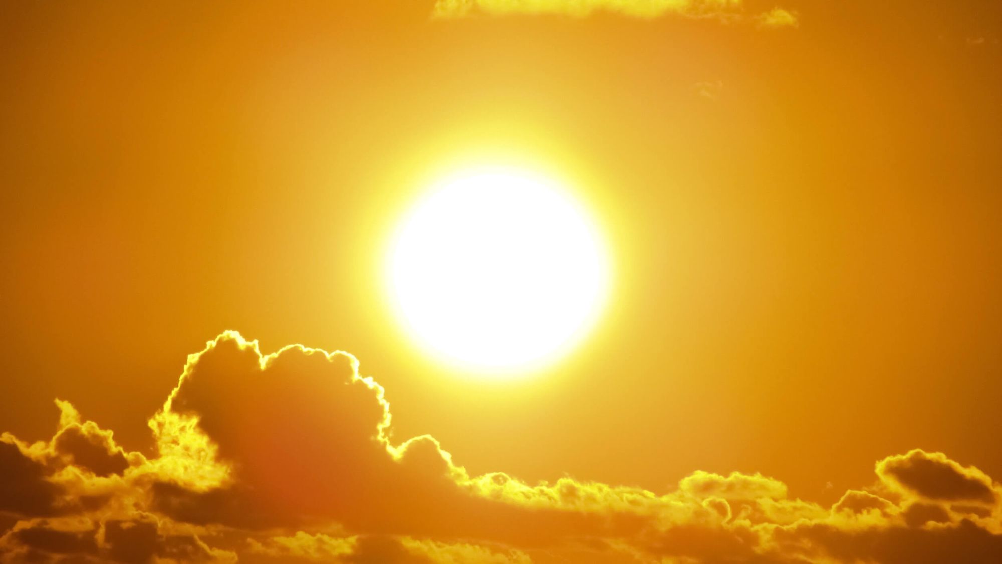 A blazing yellow summer sun above a line of clouds.