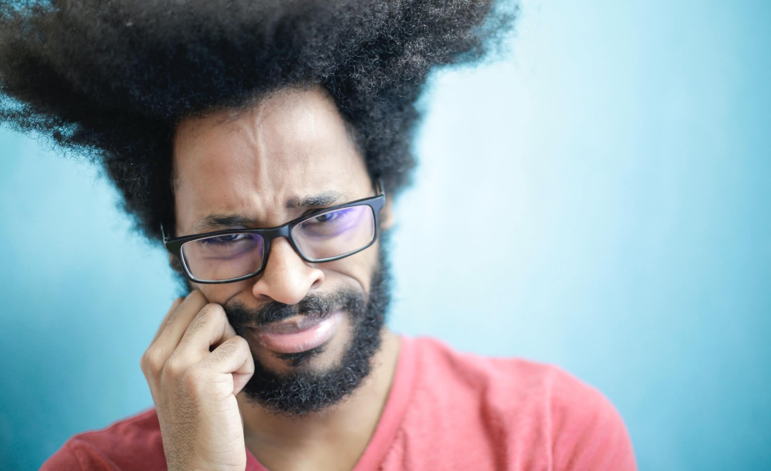Man with glasses cringing while looking at the camera.