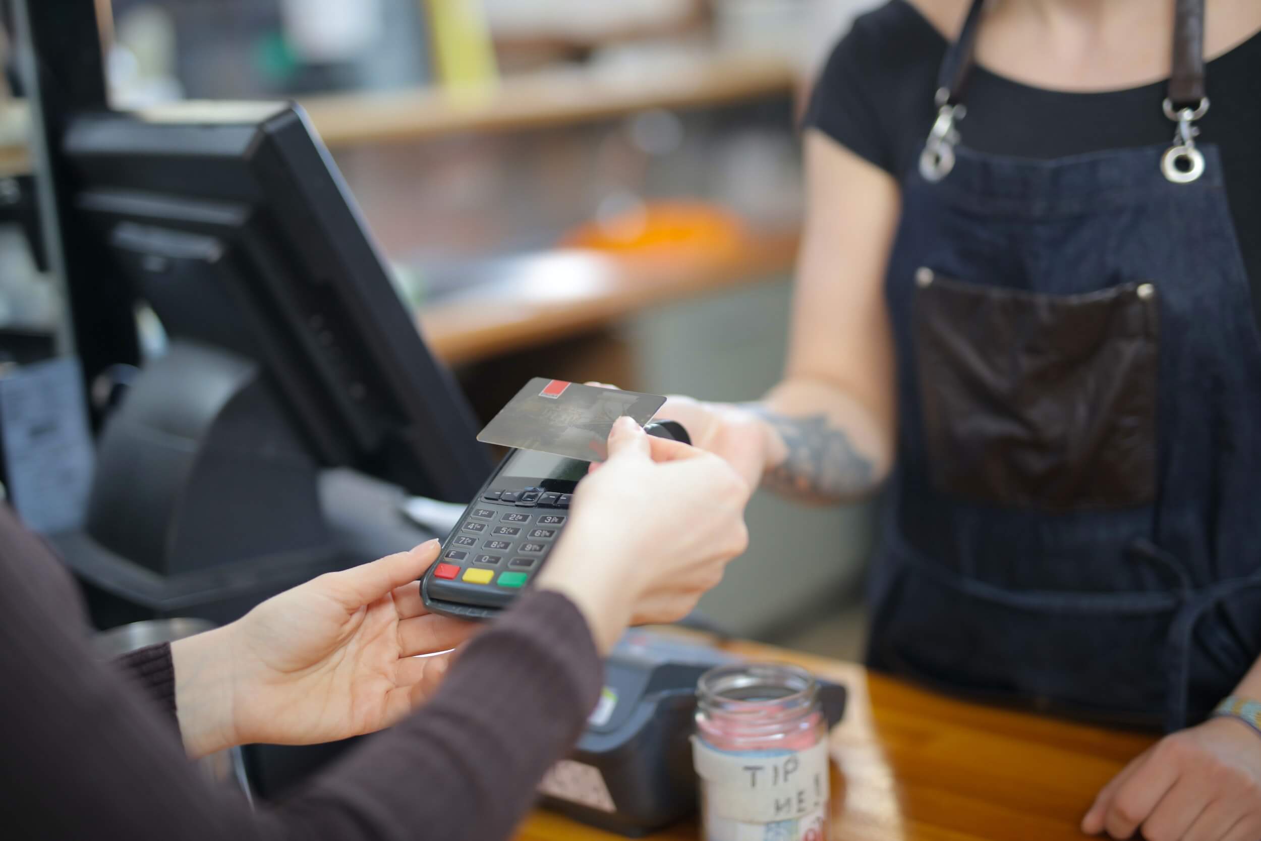 Close-up photo of a shop worker holding a debit card reader while a customer makes a payment