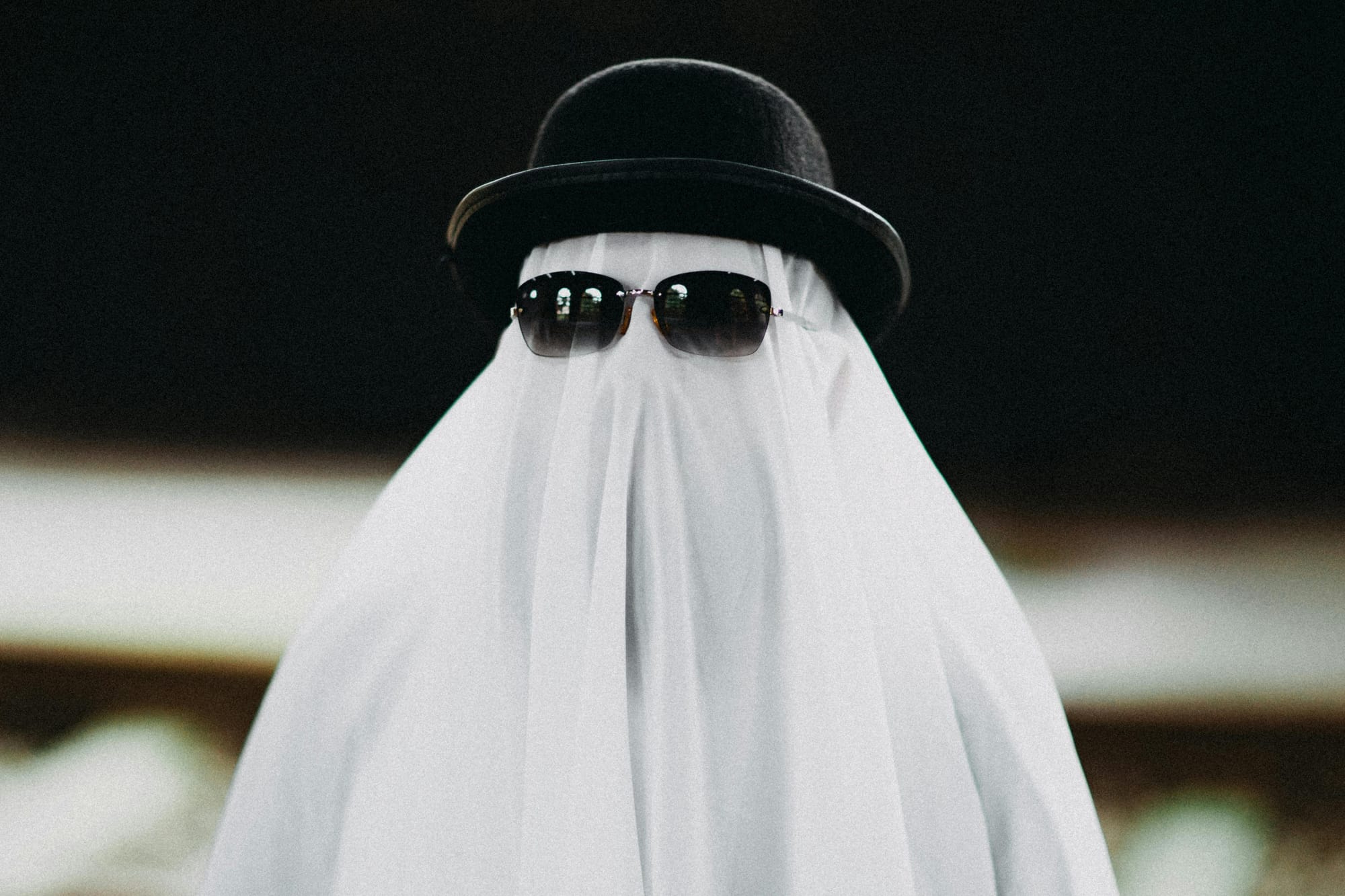 Someone covered in a white sheet to look like a ghost, with sunglasses and a bowler hat over the sheet.