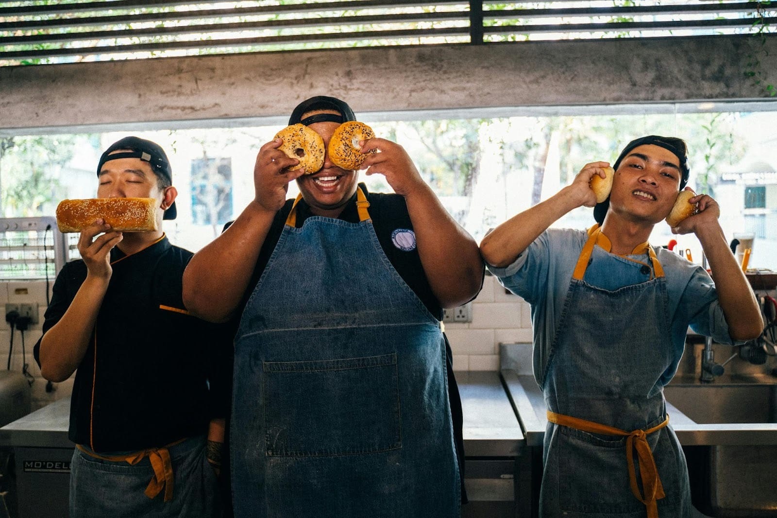 Three happy hospitality workers hold up bread products in amusement to show the 'speak no evil', 'see no evil', and 'hear no evil' symbols.