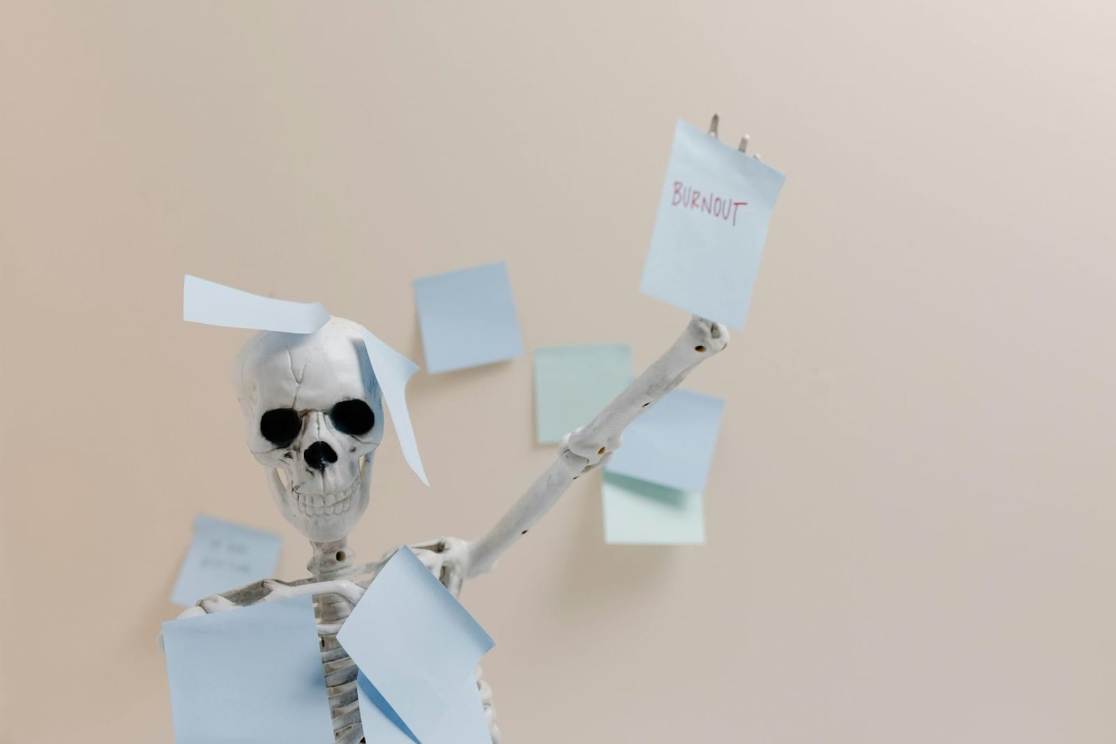 A plastic skeleton covered in post-it notes, with one hand raised to show one post-it note reading 'BURNOUT' in red handwriting.