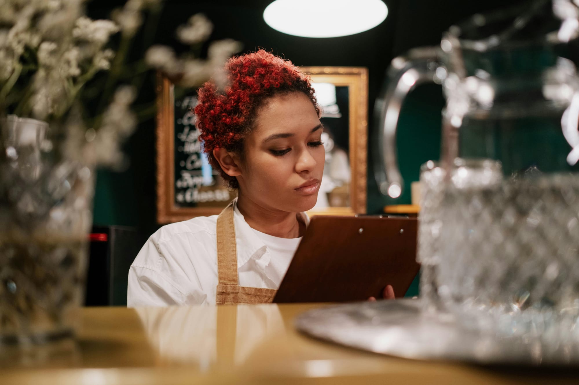 A red, short-haired hospitality worker busies herself with a clipboard behind the bar.