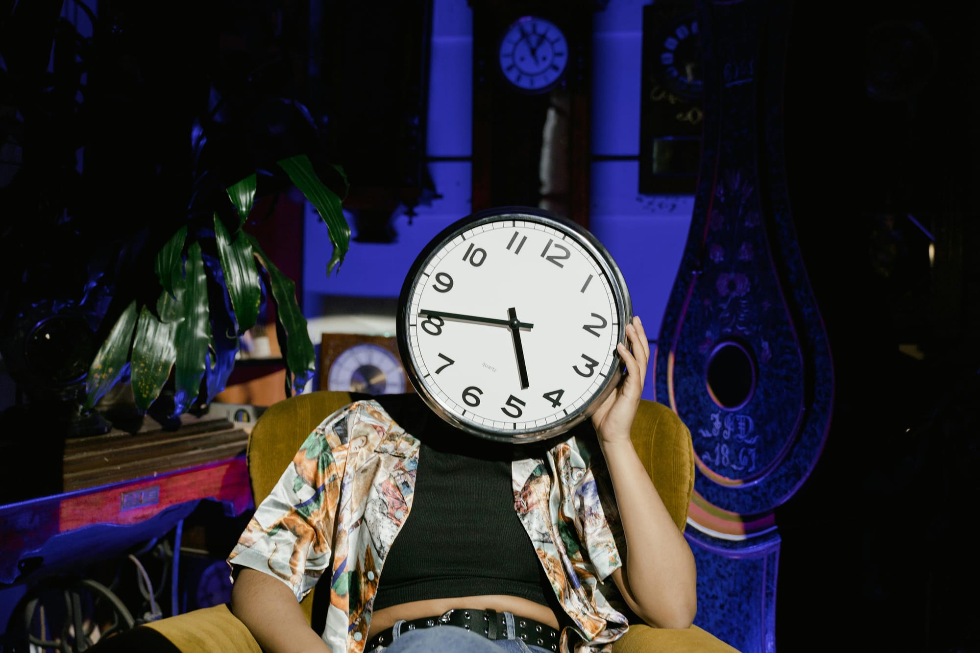 Someone with a clock for a head slumped in an armchair, leaning their clock-head into their hand.