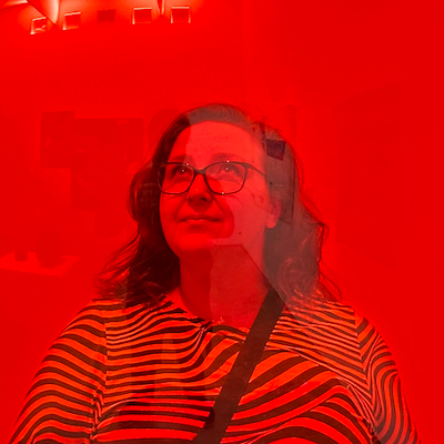 A woman in a striped dress looks upward. The whole image is shot through red plexiglass and tinted red.