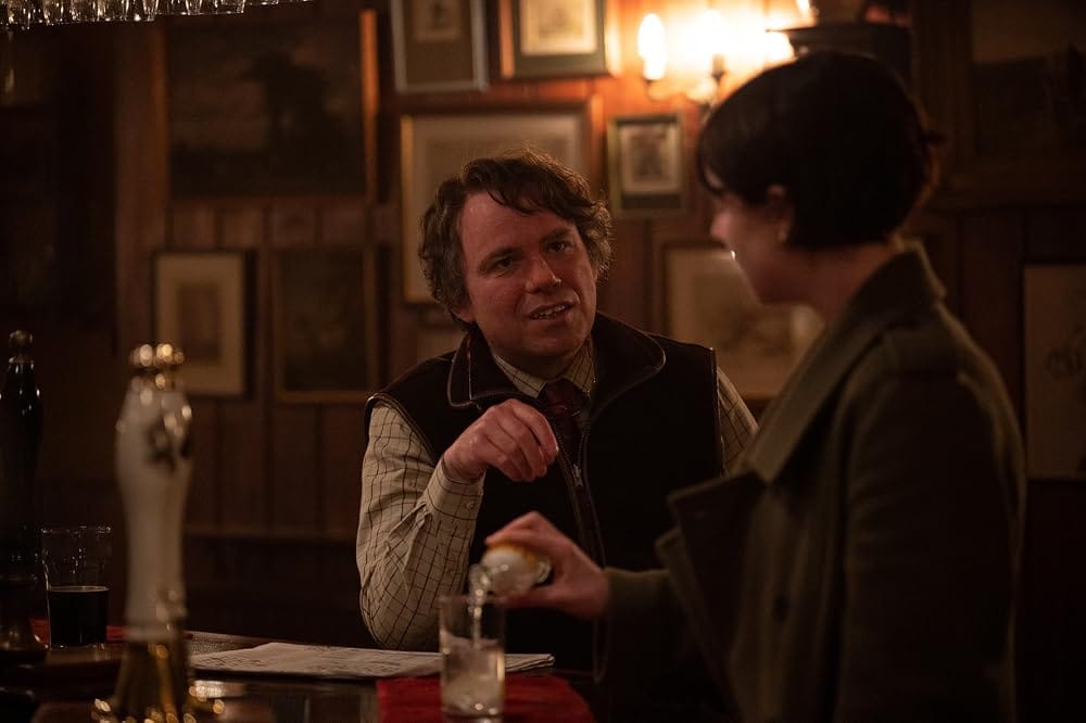 In an English country pub, Rory Kinnear and Jessie Buckley sit at the bar together
