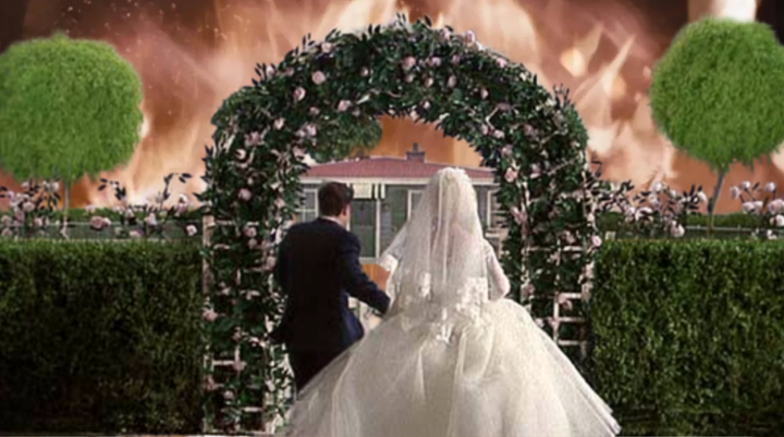A married couple runs toward an idyllic home with flames in the background. 