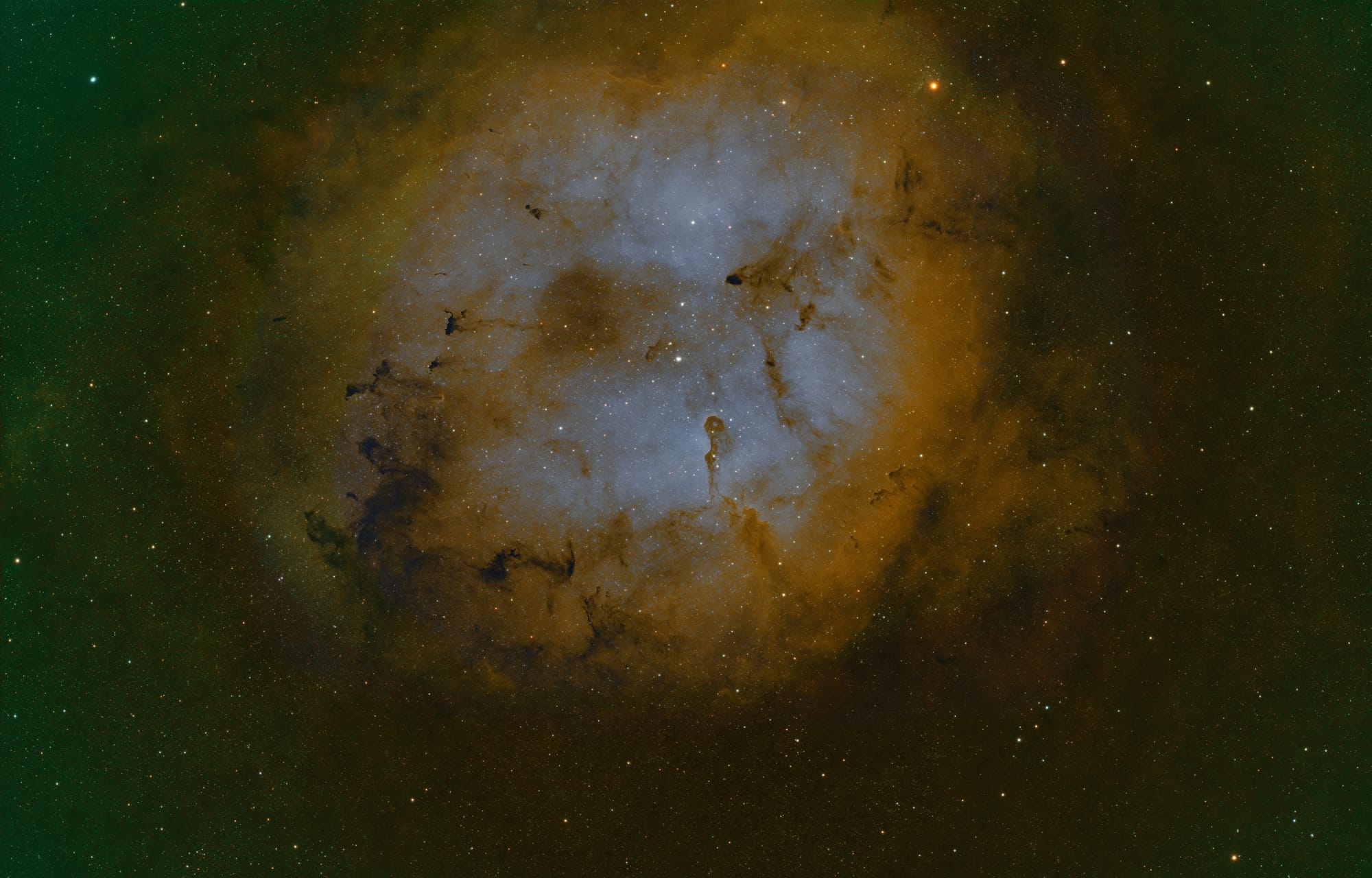 A reddish-brown circle of gas surrounding a blue nebula with a pillar of gas, resembling and elephant's trunk extending from the edge to the center