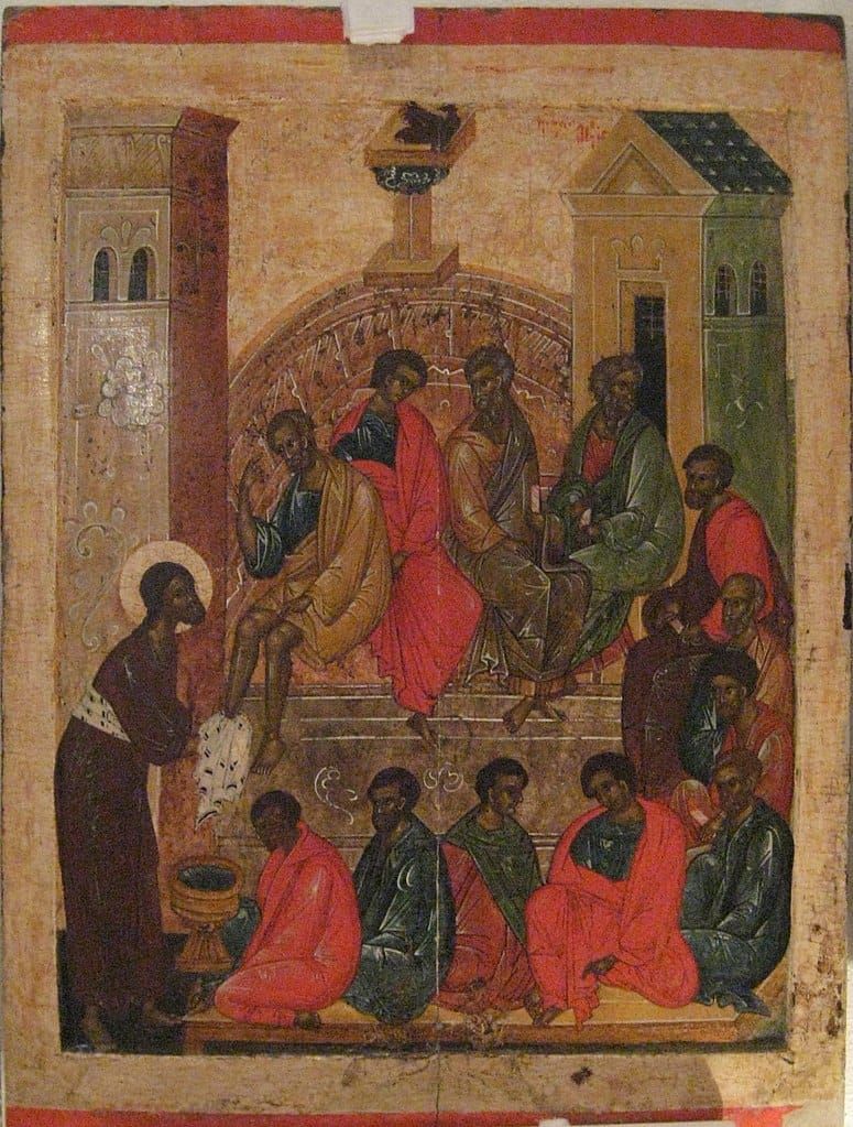 12 men sitting around a room while a haloed man washes the feet of one