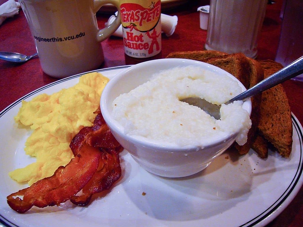 Photo of a bowl of hominy grits beside servings of scrambled eggs, bacon, and toast