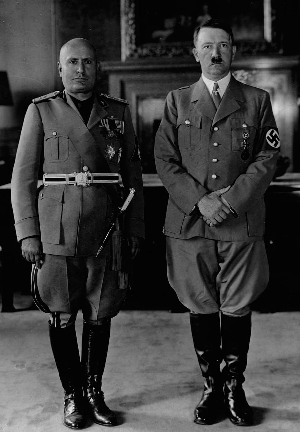 B&W photo of Benito Mussolini and Adolf Hitler, both in uniform and stone-faced, standing next to one another