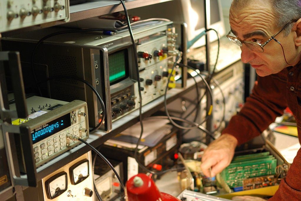 Photo of a man leaning over an electronics work bench and making adjustments to the equipment
