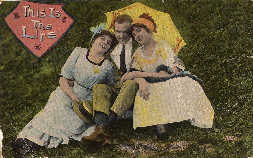 Postcard, c. 1910, depicting a man and two women seated, with his harms around the pair,  captioned, “This Is the Life”