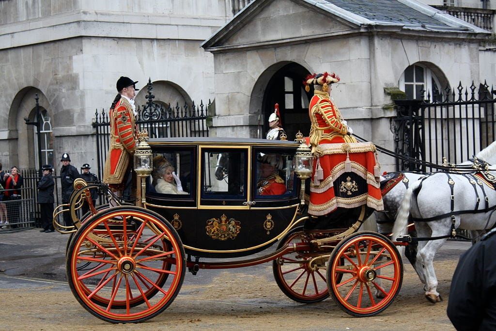 Photo of an ornate horse-drawn carriage with driver and footmen in 18th-century dress
