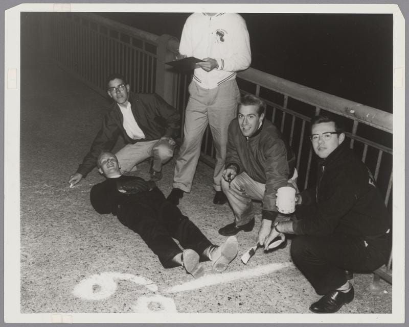 B&W photo of 5 young men measuring the length of a bridge by having one of them lie down while the others mark the distance