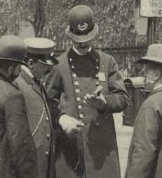 B&W photo of a policeman in 1890s uniform talking to three other men