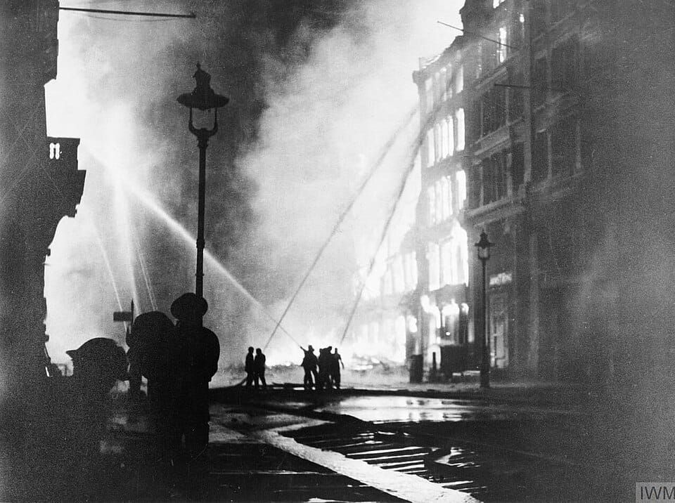 Nighttime B&W photo of firefighters battling a large fire in a city