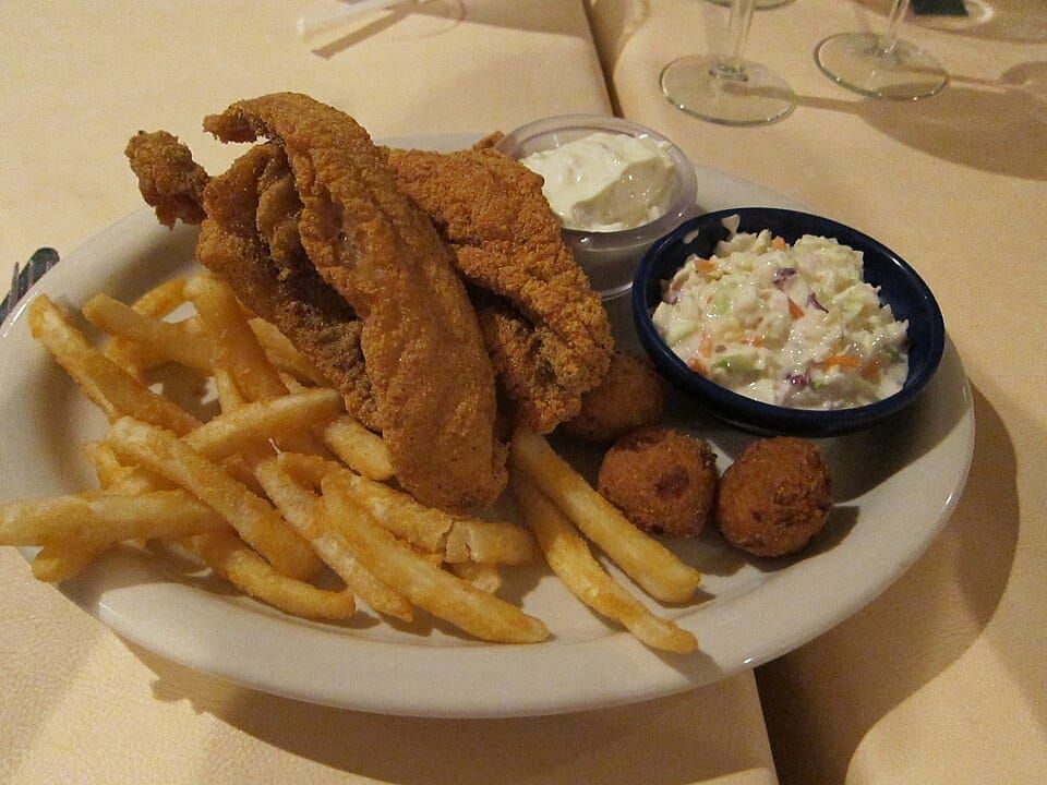 Photo of a plate with hush puppies, fried catfish, french fries, cole slaw, and tartar sauce