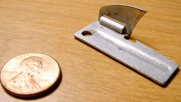 A 1.5-inch-long, steel can opener next to a penny for size comparison