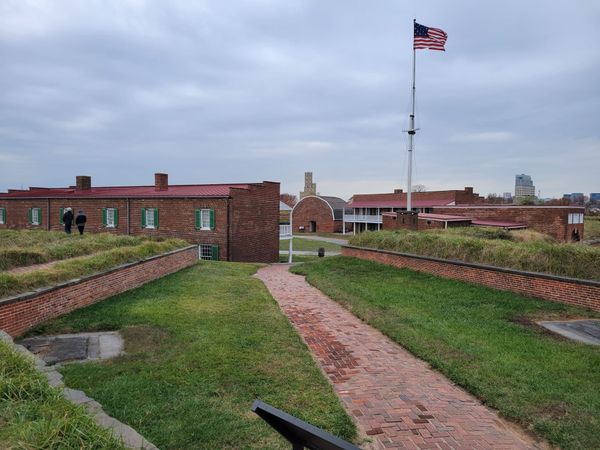 An early 19th-century fort, brick buildings surrounded by earthen battlements, with a 15-star American flag flying overhead