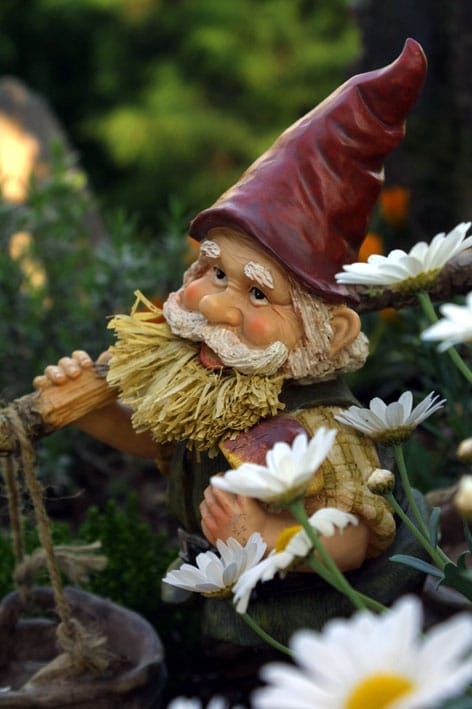 A statue of gnome with a tool slung over his shoulder, nestled among some flowers