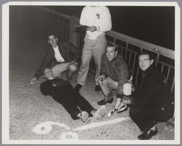 B&W photo of 5 young men measuring the length of a bridge by having one of them lie down while the others mark the distance