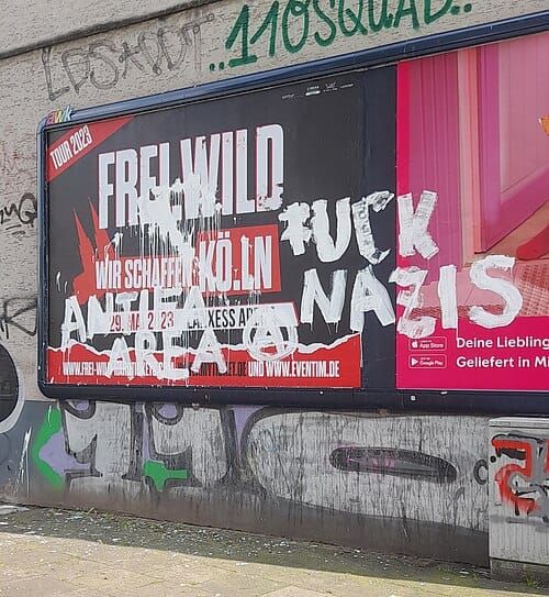 Photo of a concert billboard for the band Frei.Wild with graffiti reading “Fuck Nazis” and “Antifa Area”