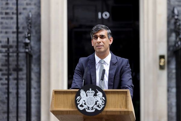 A desi man in a suit standing at a lectern in front of 10 Downing Street, London