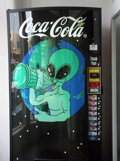 Photo of a Coca-Cola vending machine bearing the image of a green extraterrestrial drinking a bottle of Coke