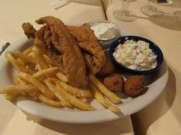 Photo of a plate with hush puppies, fried catfish, french fries, cole slaw, and tartar sauce