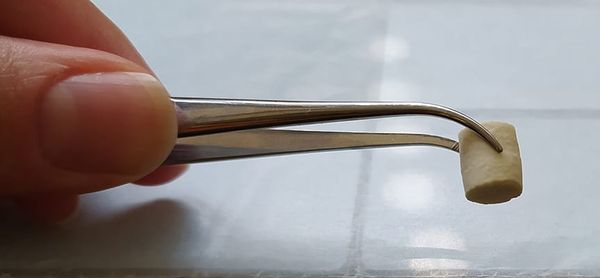 Photo of a hand holding a pair of tweezers that is picking up piece of ceramic
