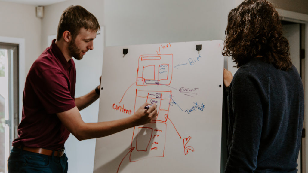 Two people standing, drawing designs on a board.