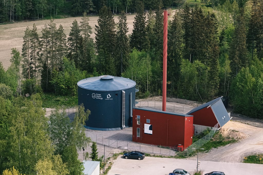 Aerial view of large cylindrical tank alongside two smaller industrial building, set in a forest clearing