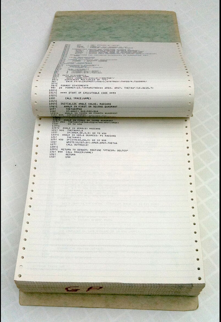 Photo of a stack of fan-fold computer paper with computer program text on opened pages