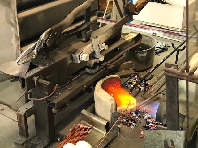 A cluttered hot-glass workbench in Murano, Italy. A glass artist is making ornamental "murrine" out of pulled glass cane.