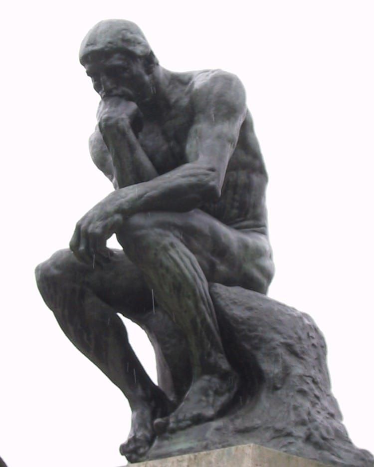 Bronze sculpture of a seated man, bent over in a pensive posture with chin resting on right hand