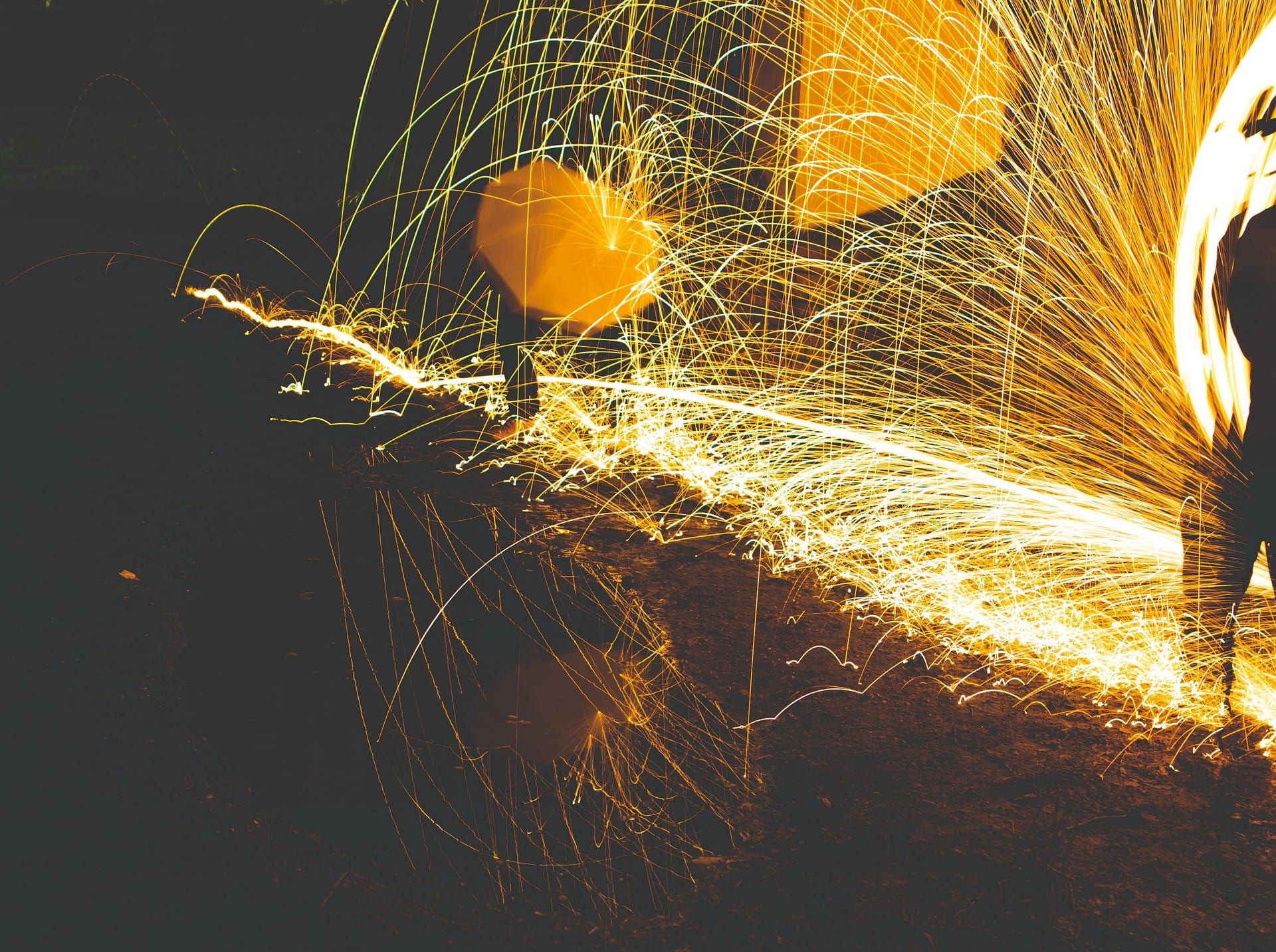 Night-time photo of bright spark trails given off by burning steel wool bundles being whirled around.