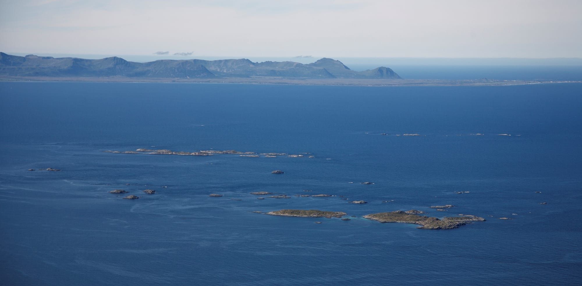 Aerial view of Andfjorden shows small islands in the foreground and mountain fjords in the distance. The water and air look cold.