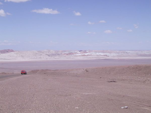 Red truck descending a long hill into a dry valley in the Atacama Desert, low barren mountains in the background