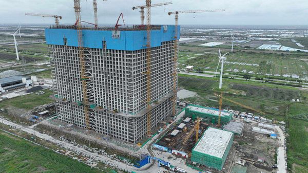 Very large cube-shaped building, about 100 metres per side, under construction, with wind turbines on flat land  in the background